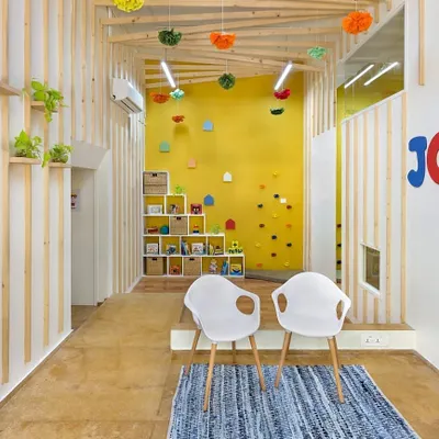 A view of the JOY Preschool and Daycare Centre in Mumbai. This area is designed to be flexible, serving as a welcoming entrance, a parent meeting spot, and a reading nook. The furniture is custom-designed with rounded edges for safety and scaled appropriately for young children.