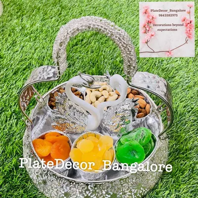 An ornate silver basket with swan figurines, filled with different compartments of dry fruits like cashews, almonds, and candied fruits.