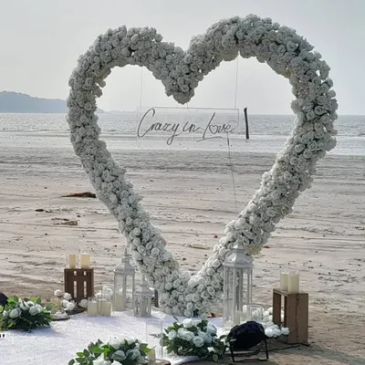 A close-up of our 'Crazy in Love' beach proposal decor. The large floral heart arch, surrounded by lanterns and candles, creates a stunning frame for the big question.