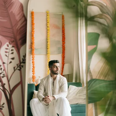 A quiet moment of reflection for the groom, Kapil, before his engagement. The mirror shot adds a creative layer, and the soft lighting creates a calm, artistic mood.