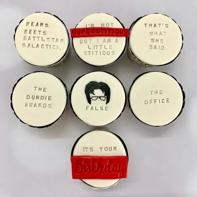 An overhead shot of "The Office" themed cupcakes, showcasing the detailed fondant work with quotes like "That's what she said" and "Bears. Beets. Battlestar Galactica."