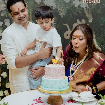 A beautiful family celebrating a baby shower. The mother-to-be is blowing out the candle on a two-tiered pink and blue cake, a sweet moment of anticipation.