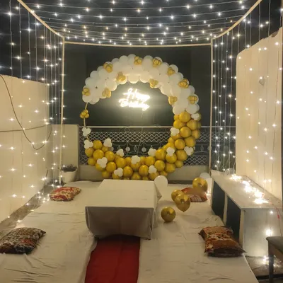 A beautiful cabana-style terrace decoration for a birthday, featuring a canopy of fairy lights, low seating with mattresses, and a crescent-shaped balloon arch.