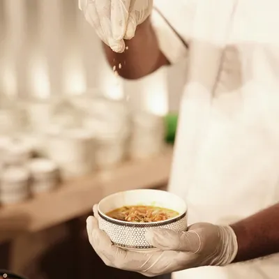 A chef adds the final garnish to a bowl of Burmese Khow Suey. This coconut-infused noodle soup is a customizable delicacy, allowing guests to add their own fresh and fried toppings for a personal touch.