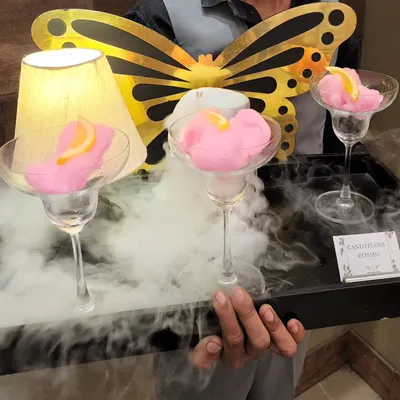 Our beautiful Candyfloss Cosmo is a visual treat. Served in a martini glass with a puff of pink candy floss, it's presented on a tray with billowing dry ice smoke.