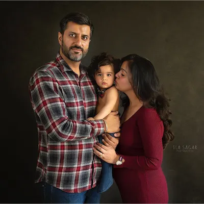 A warm and intimate family portrait. The dark background helps to emphasize the connection and love between the parents and their child.