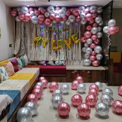 A closer view of a romantic room decoration. The 'MY LOVE' foil balloons are set against a shimmering curtain, with a canopy of balloons overhead and more scattered on the floor to create a fully immersive surprise.