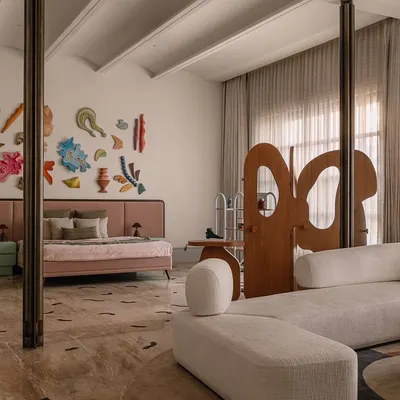 This junior master bedroom at Rehethaan is designed to feel like a private gallery. A sculptural wooden screen divides the sleeping and lounging areas, while a colorful art installation and custom furniture create a playful, sophisticated vibe.