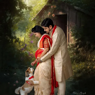 An artistic and romantic maternity portrait of a couple in traditional Indian attire, sharing a tender moment with their beloved pet in a magical, painterly forest setting.