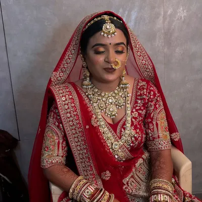 A moment of quiet elegance before the ceremony begins. This North Indian bride looks serene with her classic red lehenga, intricate jewelry, and perfectly blended HD makeup.