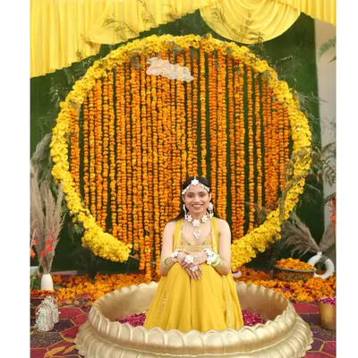 A happy bride at her Haldi ceremony, seated in front of a magnificent circular backdrop made entirely of fresh marigold strings. I added a neon 'Haldi' sign for a modern touch.