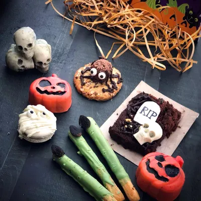 My Halloween treat box is filled with spooky delights. This flat-lay shows the full assortment: a graveyard brownie, witch finger breadsticks, a mummy-wrapped macaron, a spider cookie, pumpkin cake-pops, and edible skulls.