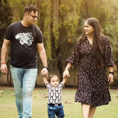 A beautiful family portrait taken outdoors, with parents holding their child's hands as he takes his first steps.