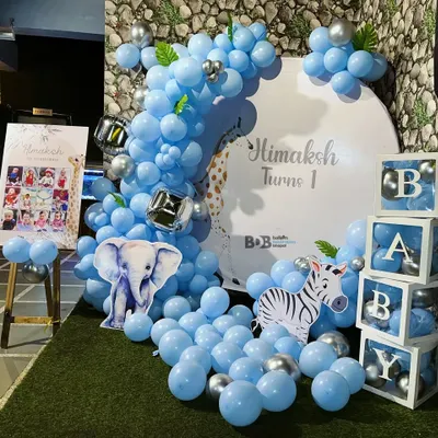 A cheerful and bright first birthday setup with a blue animal theme. This decoration includes a large balloon arrangement, cutouts of a baby elephant and zebra, and matching "BABY" display blocks.