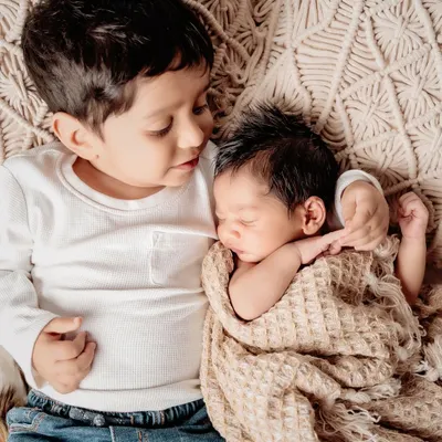 The beginning of a lifelong friendship. A big brother gently holds his sleeping newborn sibling in this heartwarming and tender portrait.