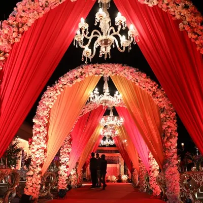 A truly royal entrance with cascading red and orange floral arches and crystal chandeliers. This grand walkway is designed to make a statement.