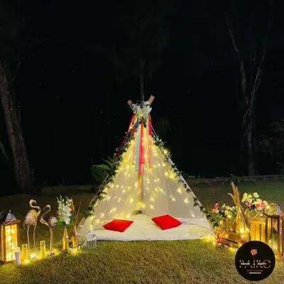 A magical teepee tent setup in a garden at night. It's decorated with fairy lights, flowers, and ribbons, creating a perfect spot for a romantic date.