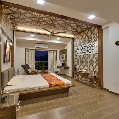 This spacious master bedroom features intricate jaali work on the ceiling and as a partition, adding a touch of traditional elegance. The low wooden bed and integrated study nook create a cohesive and luxurious space.