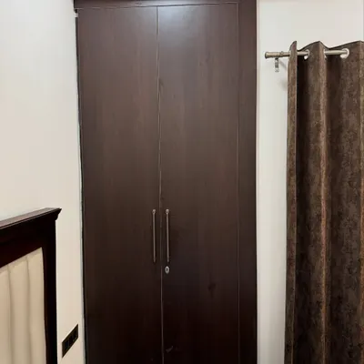 A dark wood finish wardrobe from a 2BHK apartment project in Noida Extension.
