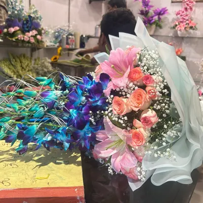 This bouquet of blue orchids, pink lilies, and roses is being prepared in my shop. You can see the freshness and care that goes into every order.