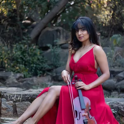 The 'Girl with Violin' concept, where the model is seated gracefully on stone steps in a woodland setting. The flowing red dress and the violin create a portrait that feels like a scene from a romantic painting.