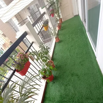 A long apartment balcony is instantly upgraded with a full carpet of artificial grass. It provides a soft surface underfoot and complements the potted plants along the railing.