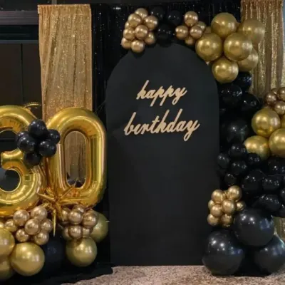 A stunning black and gold 30th birthday setup. This decor features a large foil number '30', a black arched backdrop, and a glamorous balloon arrangement against a gold sequin curtain.