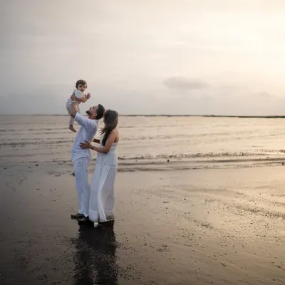 A father lifts his child towards the sky as the sun sets over the ocean. This silhouette-style shot captures a classic, heartwarming moment during a beach family photoshoot.