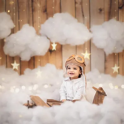 Our little pilot is ready for his first birthday adventure. Dressed in an aviator cap, this baby boy's smile lights up the whimsical cloud-filled set. This is a perfect example of a themed baby boy photoshoot.