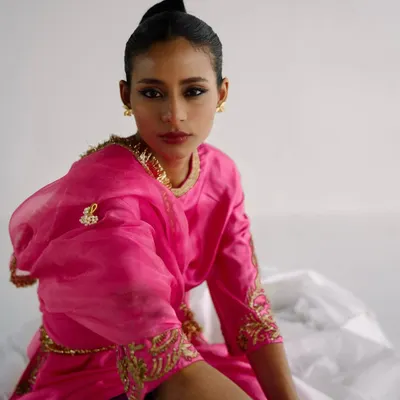 A vibrant portrait for designer Esha Arora. The bright pink of the kurta stands out against the clean white background, with a direct gaze creating an engaging image.