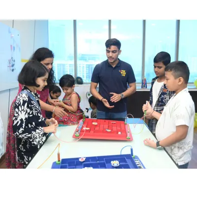 An instructor explains the rules of the steady-hand maze to a group of eager children and parents. This game tests focus and fine motor skills and is a hit with all ages.