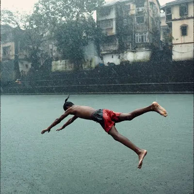 A boy captured mid-flight as he dives into the historic Banganga Tank during a downpour. This is a classic, joyful Mumbai monsoon moment.