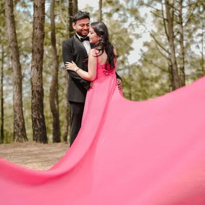 A dramatic and romantic pre-wedding portrait, using the flow of the gown's long train to create a sense of movement and artistry against the natural backdrop of the woods.