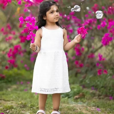 A little girl in a white dress stands in front of vibrant pink bougainvillea, with bubbles floating around her. Outdoor sessions allow for such magical, spontaneous moments.