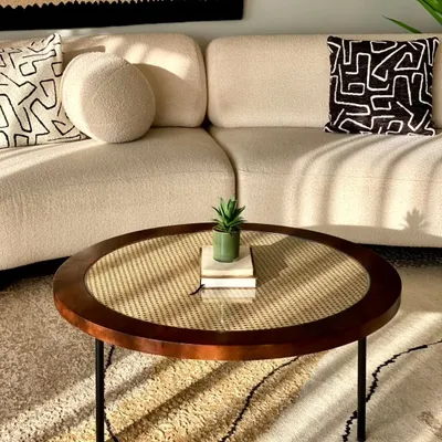 A beautiful round centre table with a dark wood frame and a natural cane weave top, protected by glass. This piece adds warmth and texture to a modern living room.