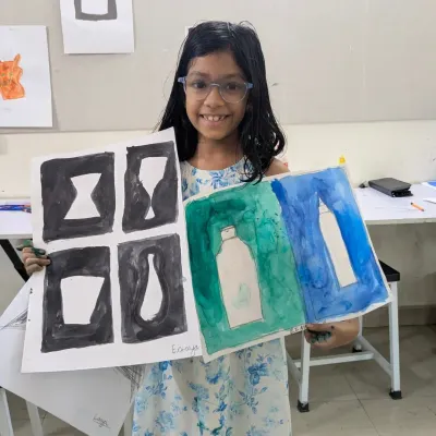 A student from our junior batch proudly displays her work from a class on negative space. This exercise trains the eye to see the shapes around an object, a key skill in composition and design.