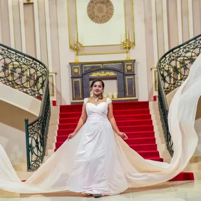 Make a grand entrance with our white trail gown. The extra long, flowing fabric adds a dramatic touch to this shot on a red carpet staircase.
