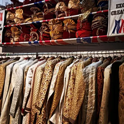 My store is packed with options. Here you can see racks filled with sherwanis in various fabrics and designs, with a full shelf of pagris and safas right above.