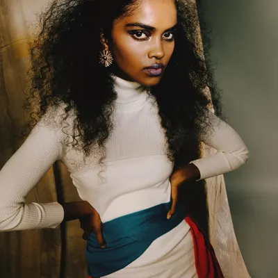 A powerful portrait from the 'ANAINA' series. The model's direct, intense gaze, combined with the voluminous hair and bold lip color, creates a captivating and confident character.