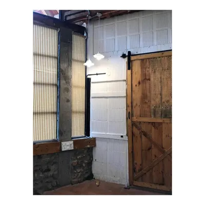 The entrance to the private farmhouse features a rustic wooden barn door and exposed stone and concrete walls. These locally sourced, natural materials set the tone for the sustainable and earthy architecture of the home.