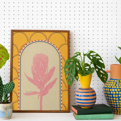 A framed print of a pink protea flower, set against a warm yellow, patterned background. This shows how my doodle style can be adapted into elegant botanical art for your home.