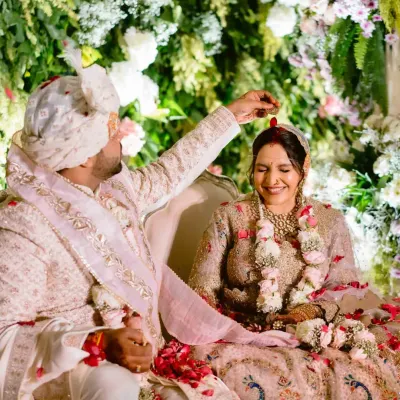 A groom gently places sindoor on his bride's forehead, a tender and significant moment during the wedding ceremony, surrounded by a cascade of flowers.