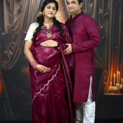A glamorous and traditional maternity portrait. The couple is dressed in beautiful ethnic wear, posing against a classic, candlelit backdrop for a regal feel.