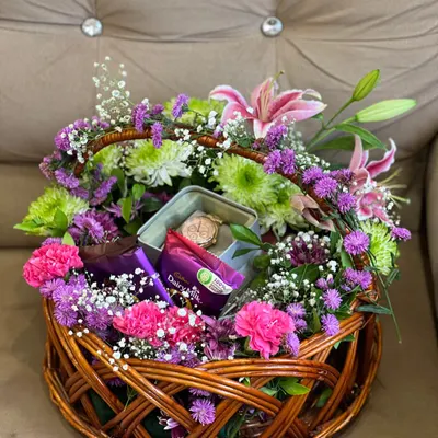 A basket of blooms that feels like a secret garden. This wicker basket is overflowing with a mix of colorful flowers and greenery, with special gifts like a watch box and chocolates hidden among the petals.