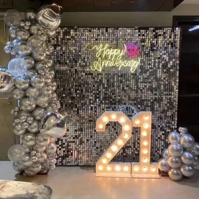 Celebrate your milestones in style. This chic 21st anniversary setup features a shimmering silver sequin wall, a custom "Happy Anniversary" neon sign, and large light-up marquee numbers for a glamorous photo corner.