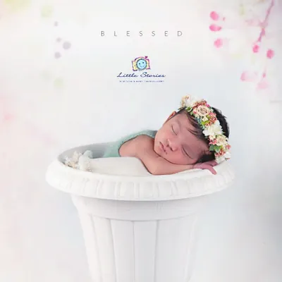 This creative shot places a peacefully sleeping baby inside a large white planter, like a little flower bud. The delicate floral crown on her head completes this charming, garden-themed portrait.