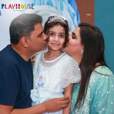A beautiful moment of family love at Sofiya's Frozen-themed party. Dressed as a princess, she gets a kiss from her parents, capturing the magic of her special day.