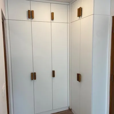 This Scandinavian-style wardrobe features custom-made handles in a natural wood veneer, providing a beautiful, warm contrast against the matte white shutters.