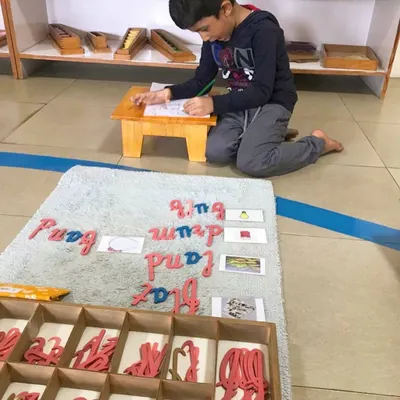 The Moveable Alphabet is where writing begins. Here, a child uses wooden cursive letters to build words, transforming his thoughts into written language before he has even mastered holding a pencil.