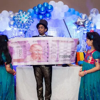 Performing a money magic trick for two young audience members at a birthday party, keeping the kids amazed and entertained.